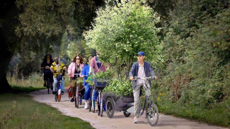 Landschapskunstenaar Bruno Doedens op de fiets met een boom achterop. Achter hem fietsen andere fietsers