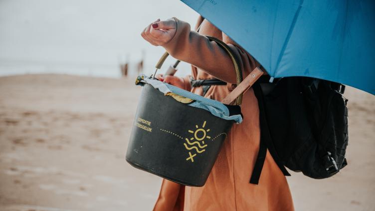 Persoon op het strand met emmer en paraplu