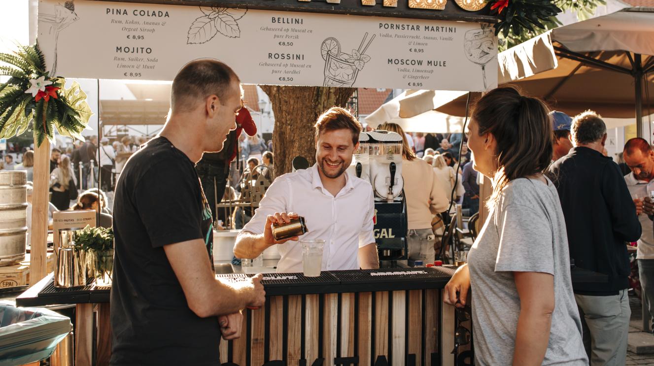 Barman maakt een cocktail in een foodtruck tijdens een evenement terwijl 2 mensen aan de bar toekijken