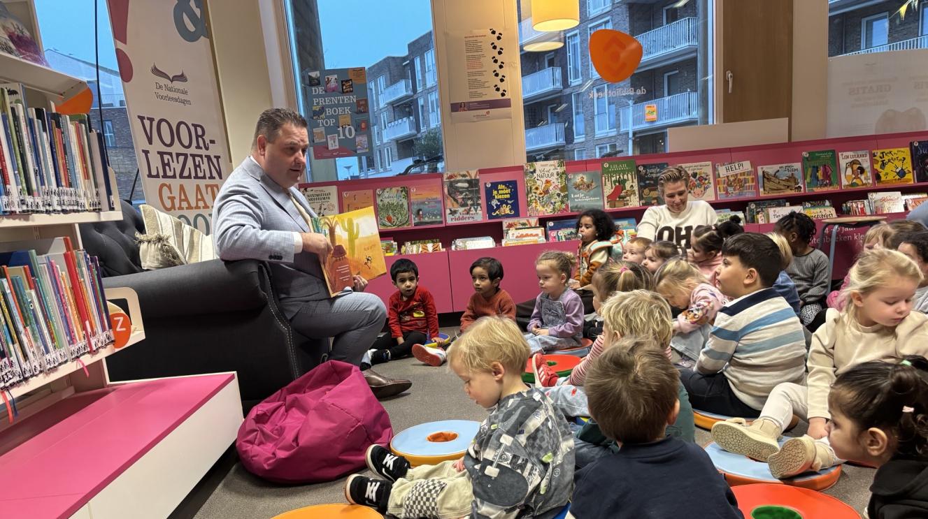 Wethouder Carree zit voor een kring van peuters en leest voor