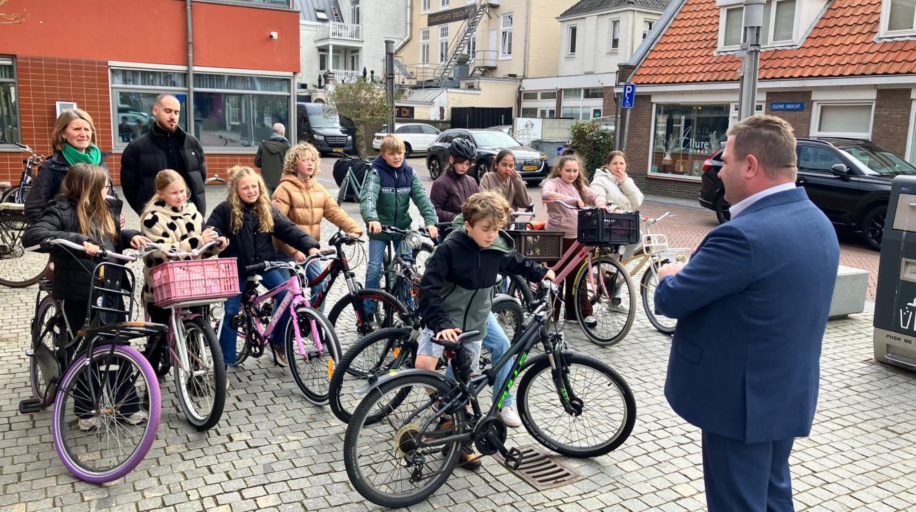Groep kinderen op de fiets voor het gemeentehuis samen met wethouder