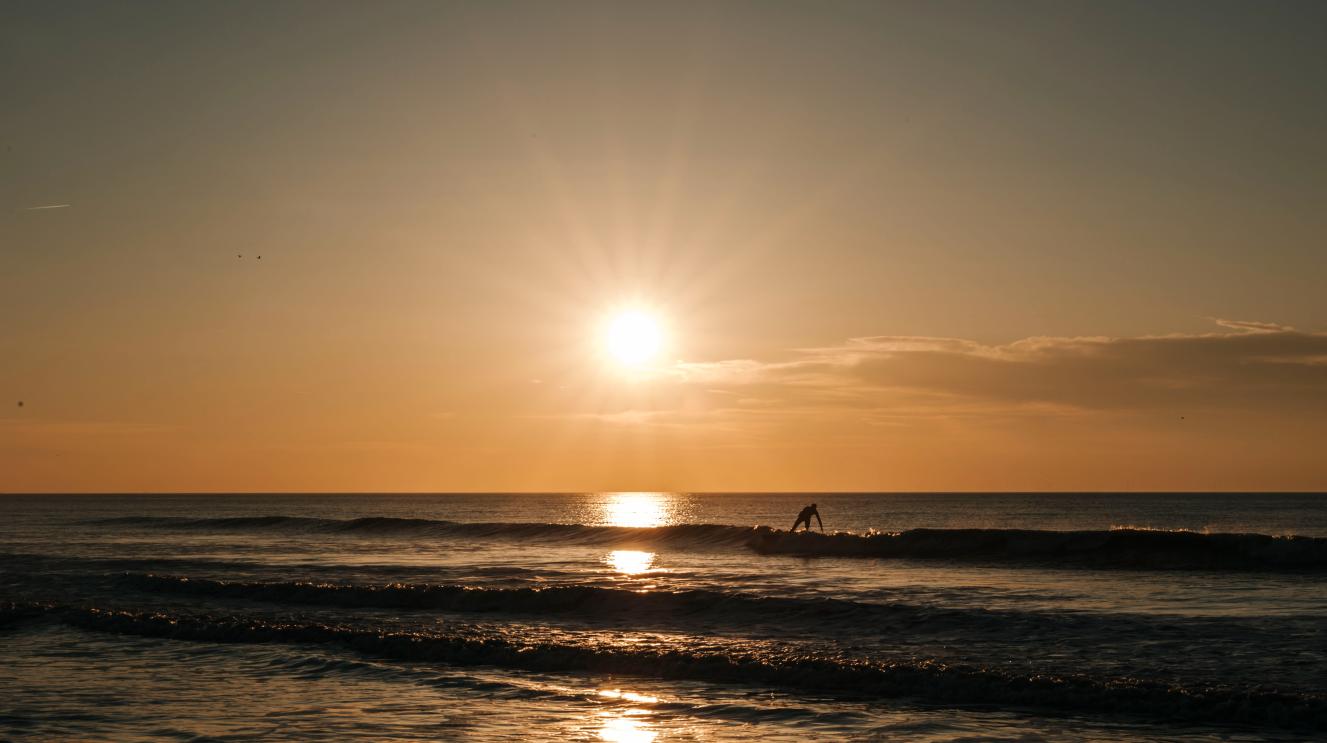 Ondergaande zon boven de zee met een surfer
