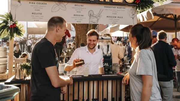 Barman maakt een cocktail in een foodtruck tijdens een evenement terwijl 2 mensen aan de bar toekijken